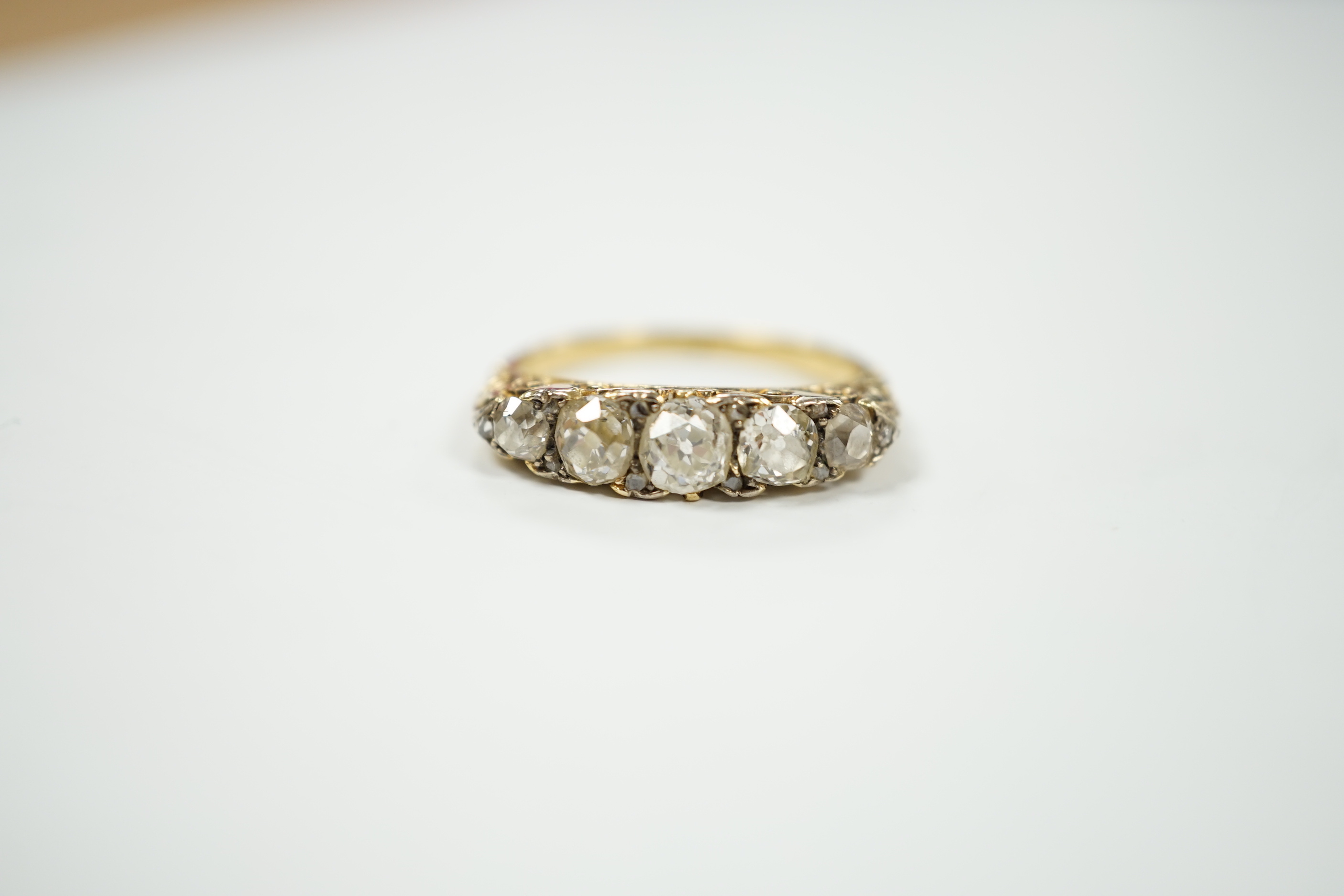 An early 20th century yellow metal and graduated five stone diamond set half hoop ring, with diamond chip spacers, size N/O, gross weight 4.7 grams.